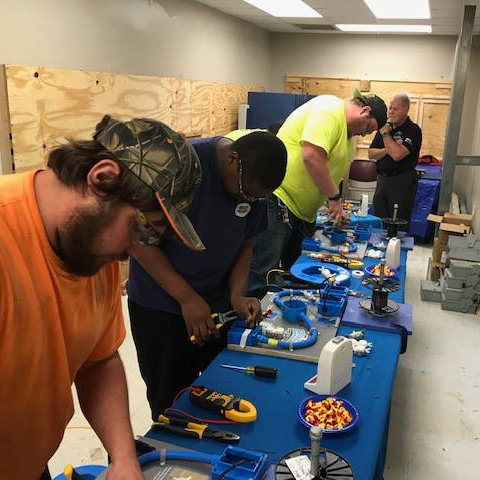 Three CECA apprentices practicing on electronic components while an instructor looks on